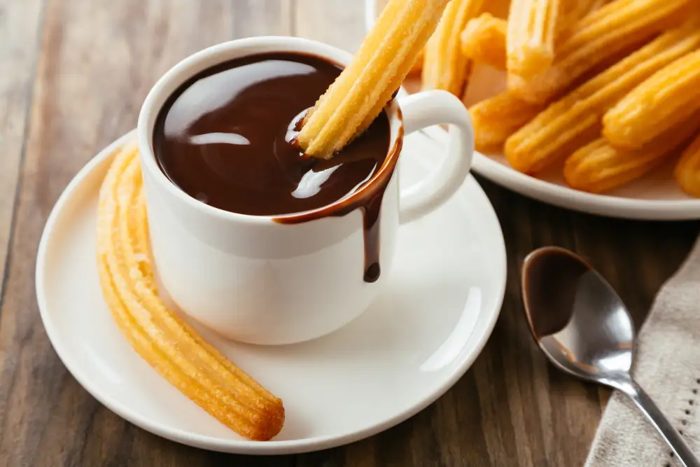 Traditionelle spanische Churros mit heißer Schokoladensauce auf einem rustikalen Holztisch