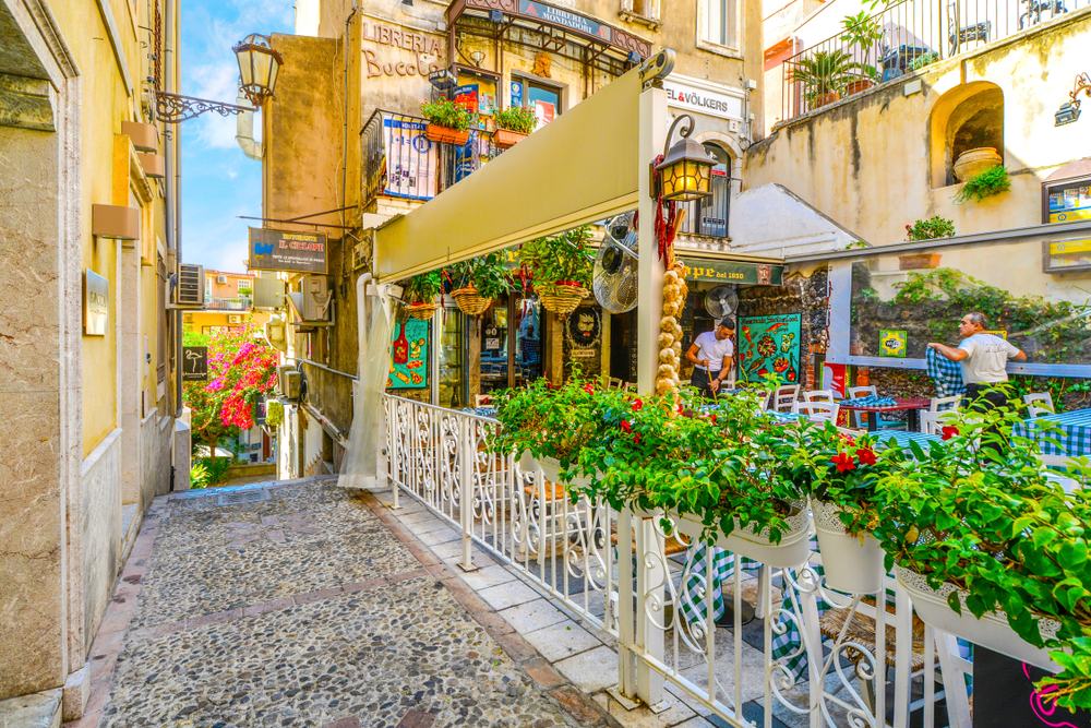 Taormina, Italy - September 15 2018: Restaurant workers prepare for the day at a colorful and picturesque cafe just off of Corso Umberto, the main street in Taormina Italy on the island of Sicily.
