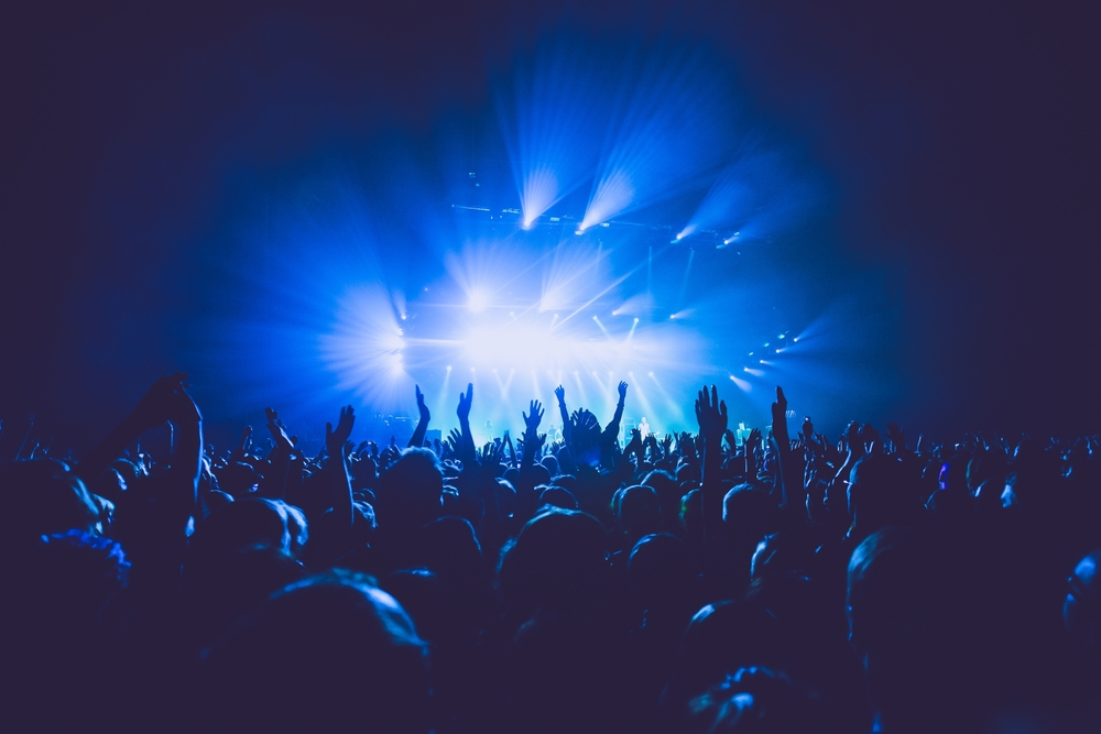 A crowded concert hall with scene stage lights in blue tones, rock show performance, with people silhouette, on a dance floor air during a concert festival