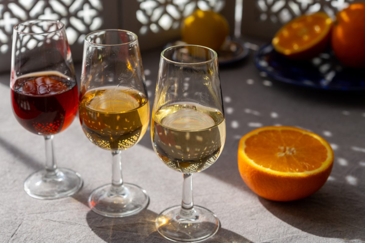 Glasses with cold dry fino and sweet cream sherry fortified wine and orange in summer sunlights, andalusian style interior on background